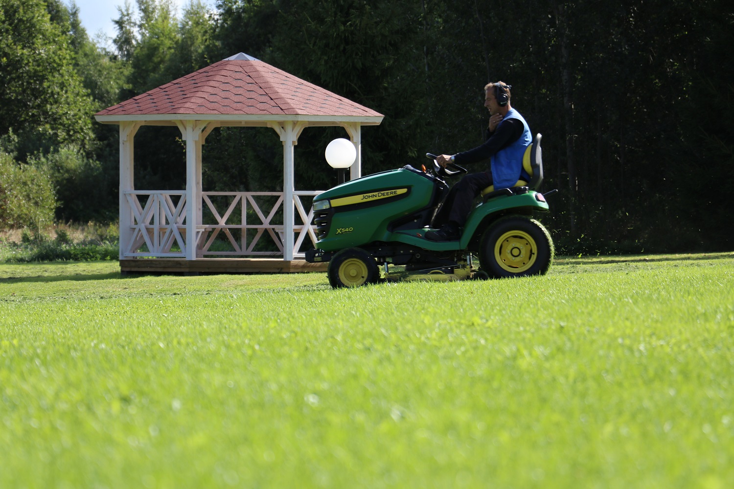 Ein Mann fährt einen John Deere Rasenmäher auf einem weitläufigen Rasen