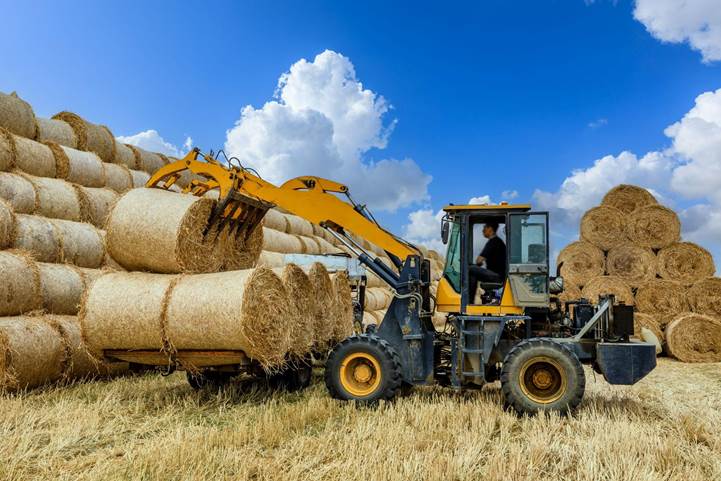 Ein landwirtschaftlicher Traktor entlädt Strohballen vom LKW
